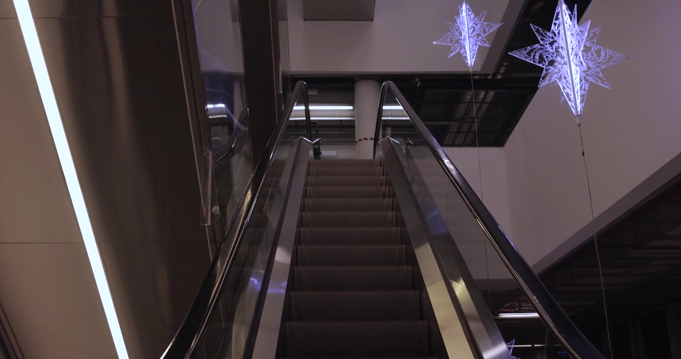 Escaleras mecánicas en un centro comercial vacío con luces de Navidad colgando. 4K