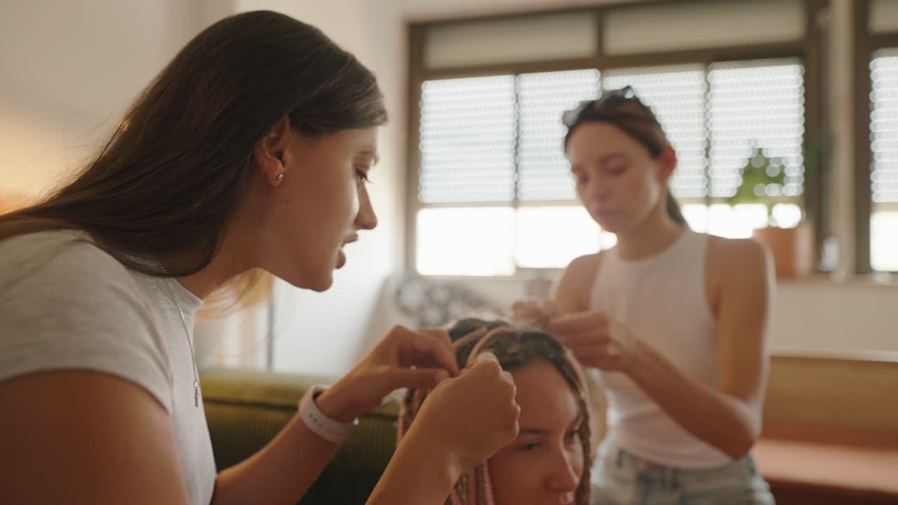 Two women braiding another woman's hair