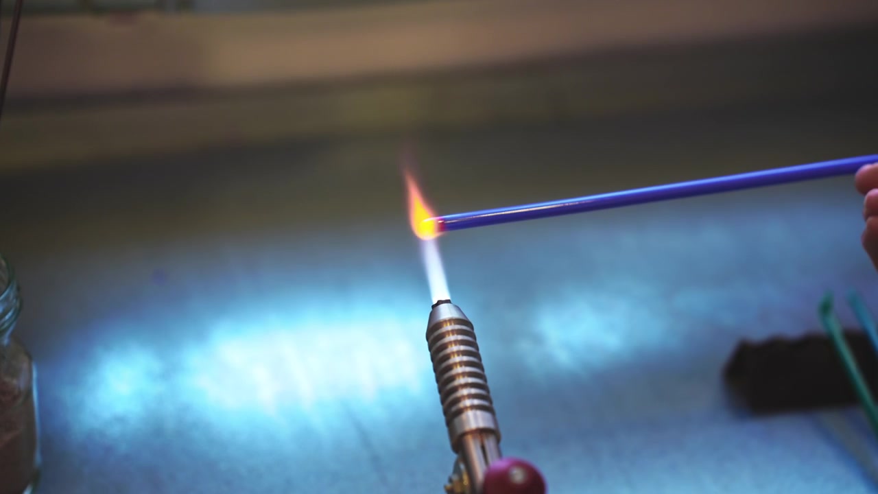Lokal håndverker som smelter glass over en blåselampeflamme for å lage tradisjonelle vikingperler. Autentisk smykkeverksted på Lofoten, Norge