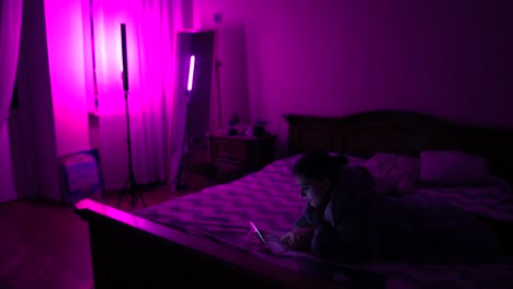 mujer usando tableta en un dormitorio iluminado de púrpura por la noche