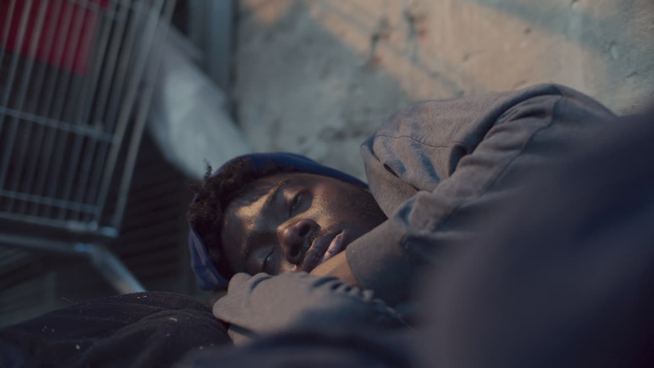 Homeless Black Man Lying on Street and Shivering from Cold
