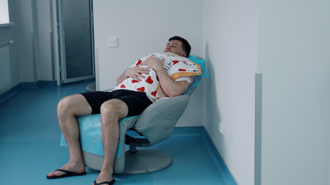 Caucasian man sits in a chair holding a newborn child on the chest. Loving dad taking care of his baby.