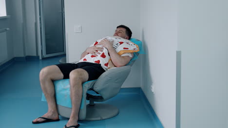 caucasian man sits in a chair holding a newborn child on the chest. loving dad taking care of his baby.