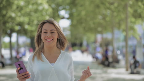 Mujer-Joven-Emocionada-Usando-Un-Teléfono-Inteligente-Al-Aire-Libre