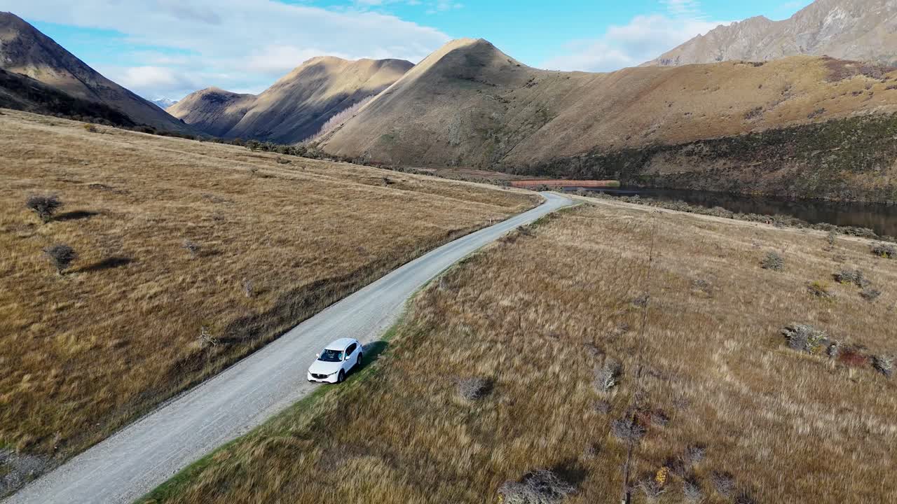 Aerial view of a vehicle traveling through Queenstown's rugged terrain, showcasing expansive mountain views and clear skies
