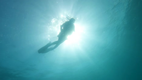 Cinematic-underwater-shot-of-a-scuba-diver-in-clear-waters-with-the-sun-in-the-background,-4K,-120FPS,-Slomo