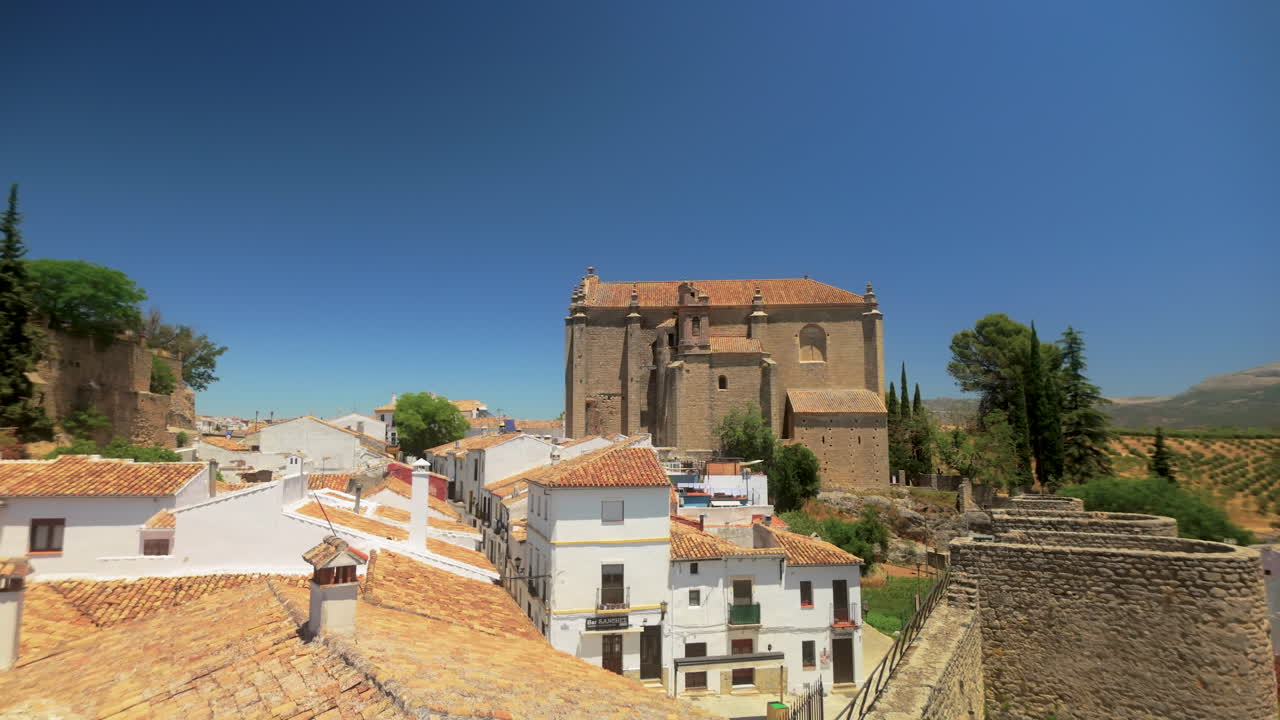 Vista dai tetti del centro storico di Ronda con case tradizionali spagnole e una grande chiesa. Il cielo azzurro limpido esalta il fascino della città.