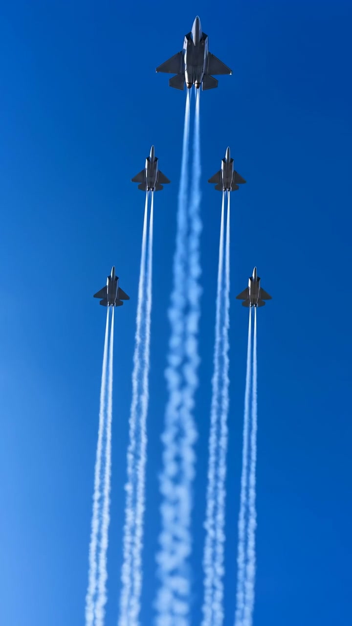 Cinque aerei a reazione scuri si muovono verso l'alto in formazione simmetrica mentre scie bianche brillanti si allungano dietro di loro, creando forti linee verticali contro un cielo blu senza nuvole