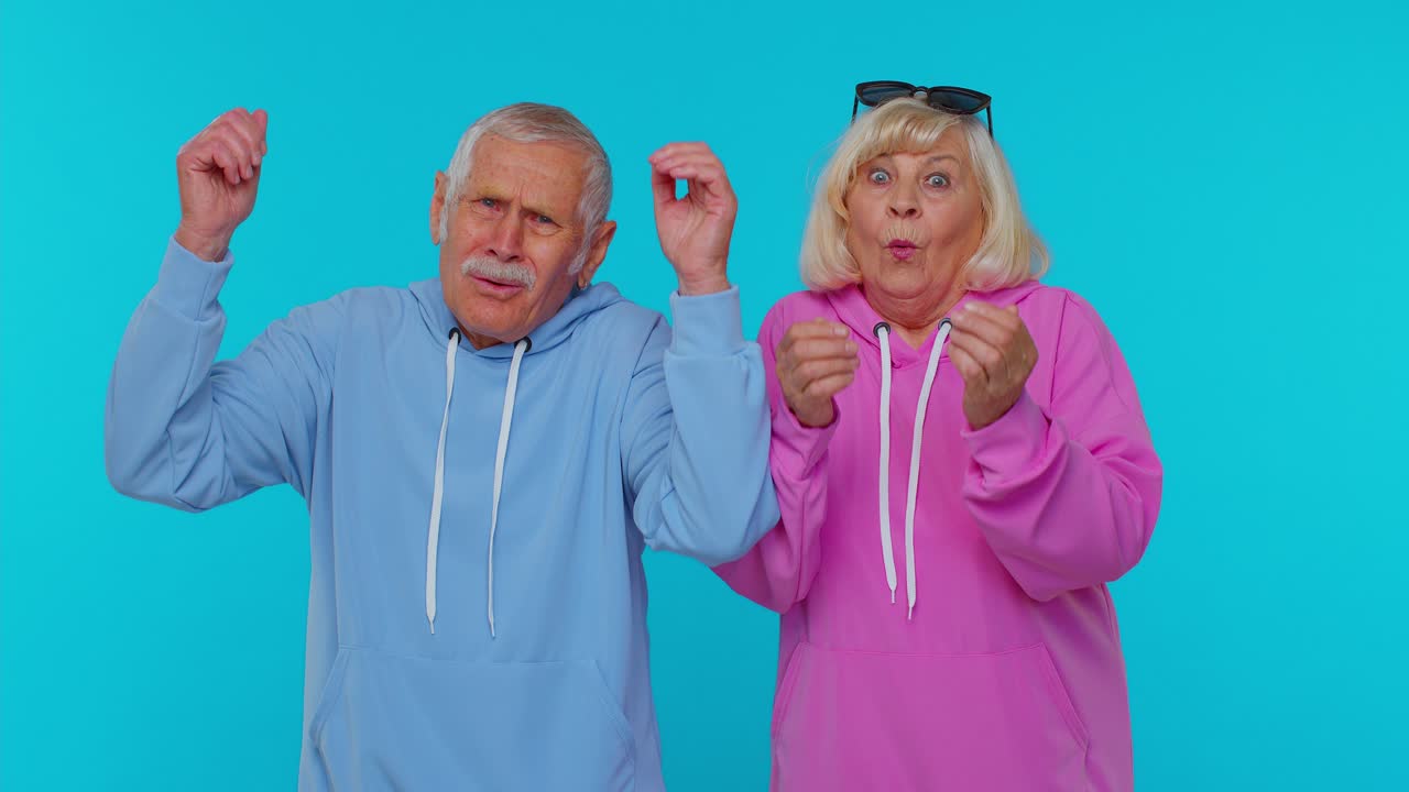 Excited amazed grandfather grandmother pensioners raising hands in surprise win shocked by victory