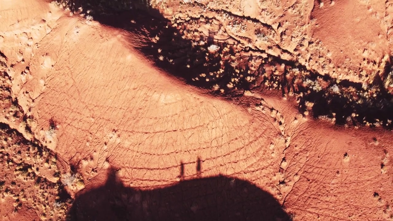 Vista dall'alto con drone della silhouette di una coppia che cammina su una cresta di arenaria rossa nei canyon di Konorchek, Kirghizistan. Prospettiva unica di viaggiatori nel paesaggio desertico arido dell'Asia Centrale