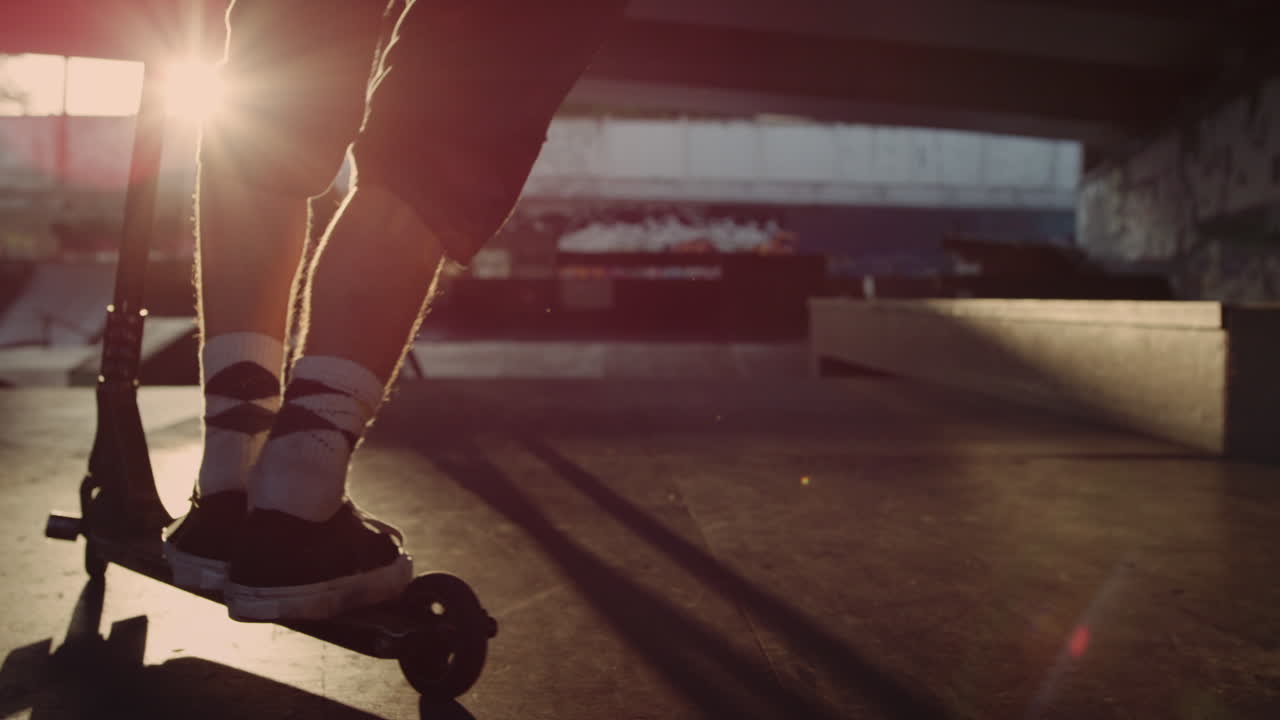 Extreme teenager training skills on scooter at sunset city skate park.