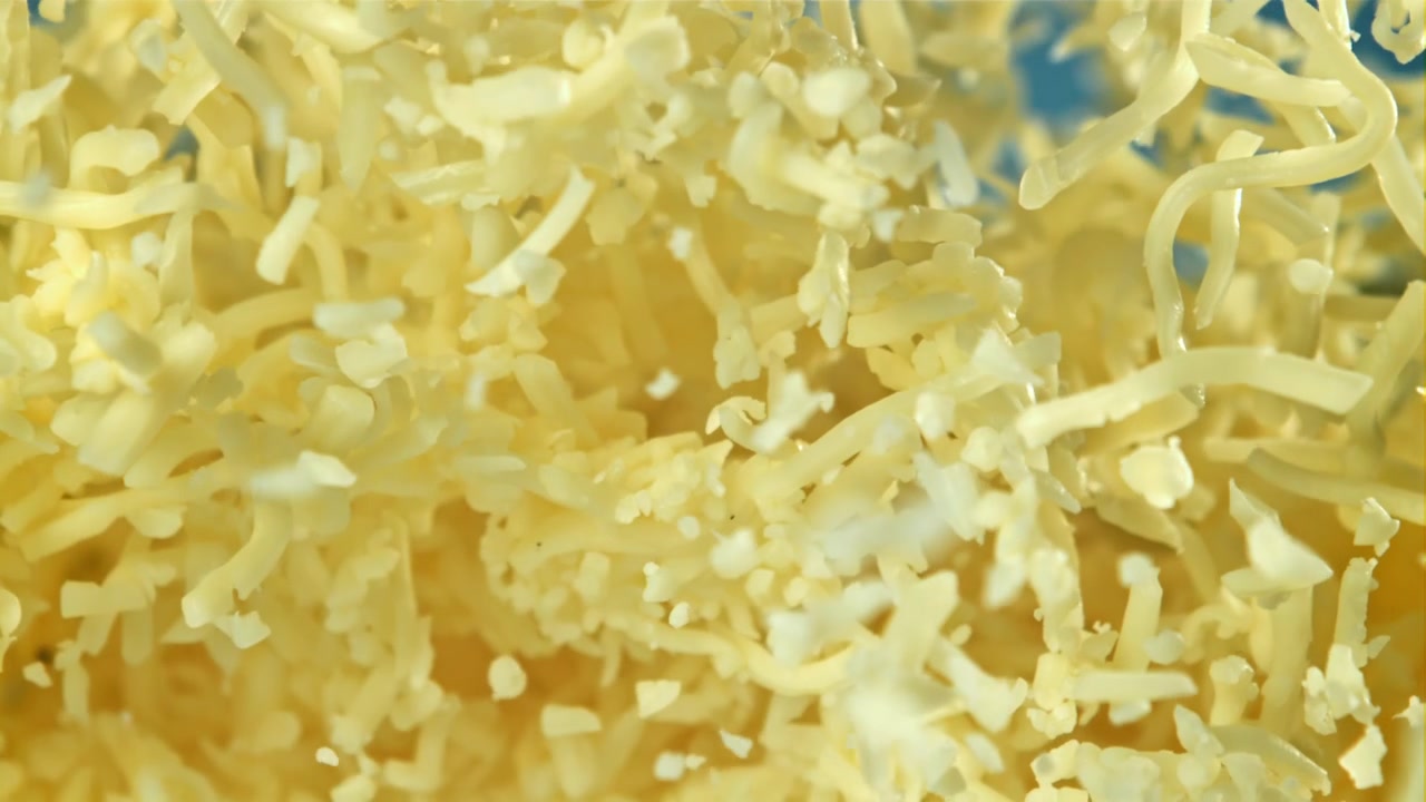 Shredded Cheese Falling in Slow Motion Against a Blue Background