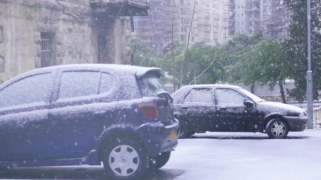 Two parked cars in urban inner city Jerusalem city with snow falling, slow motion