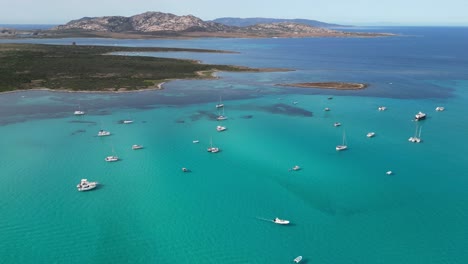 boats floating at turquoise blue sea near isola piana island, la pelosa, sardinia, italy - aerial 4k circling