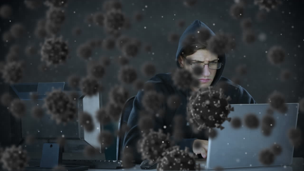 Animation of of macro covid19 cells over man wearing hoodie, using a laptop