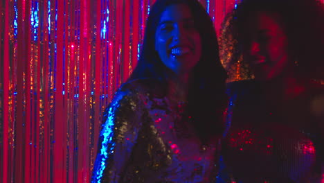 portrait of two women friends having fun in nightclub or bar dancing against sparkling tinsel curtain in background