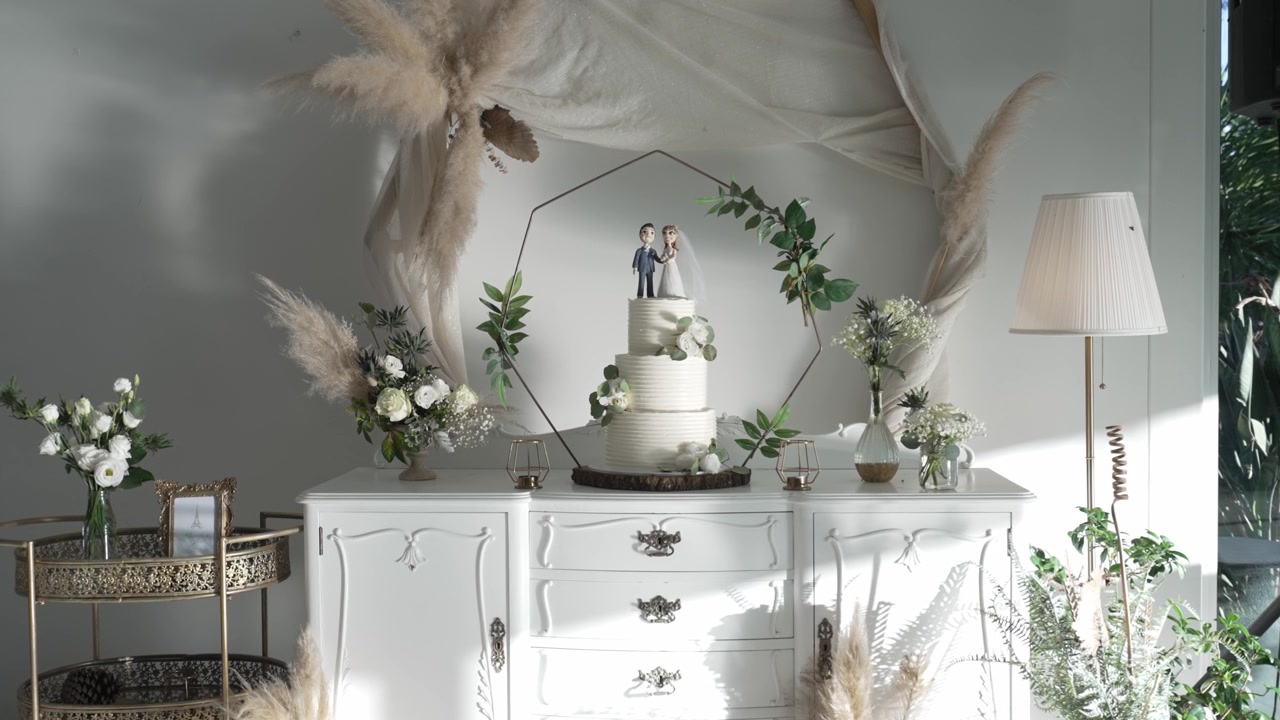 Tavolo elegante per torta nuziale con decorazioni floreali, erba della pampa e uno sfondo geometrico