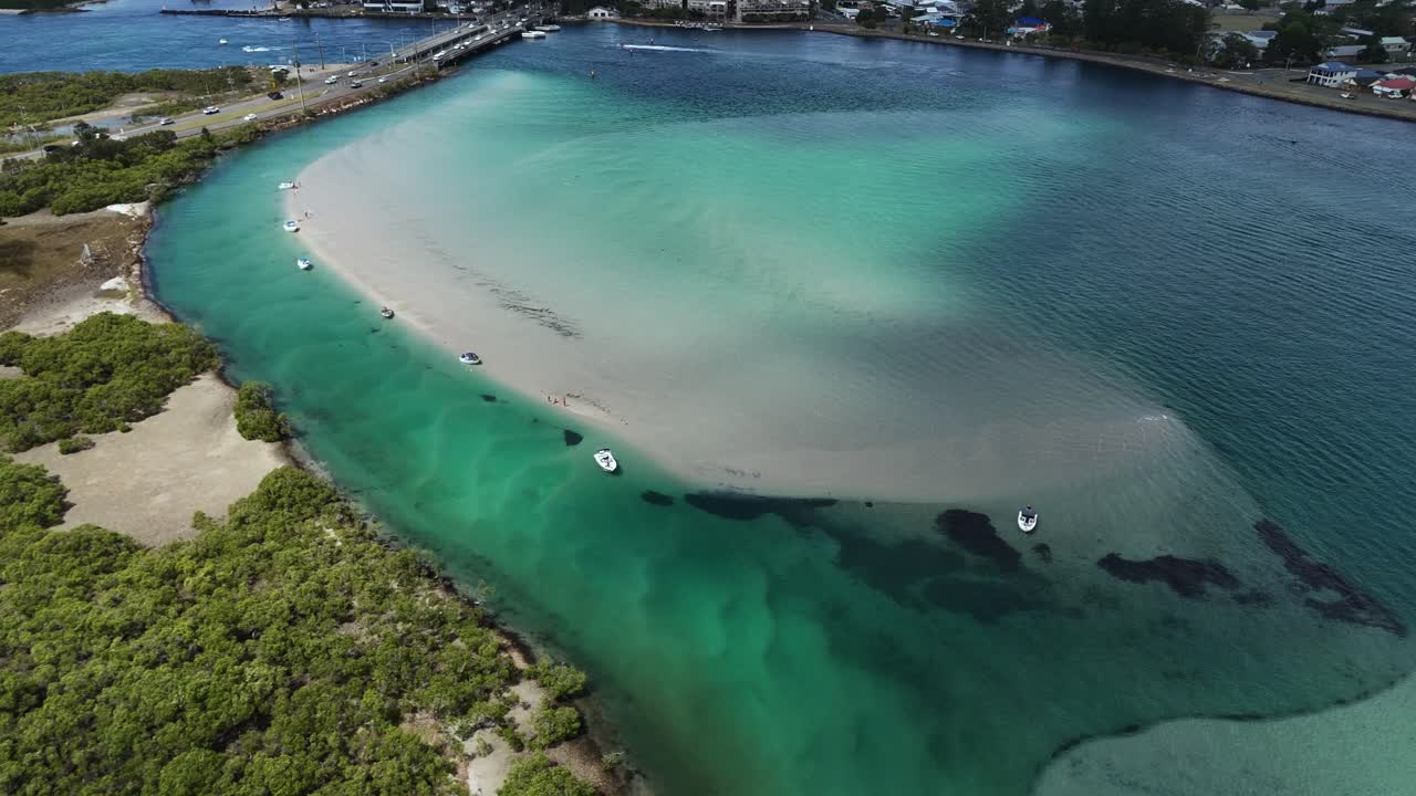 Drone orbit of Swansea lagoon with bright shallow water and boats along sandy edges