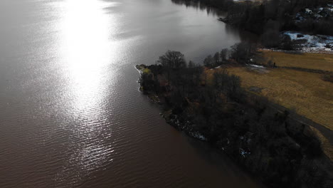 sunlight reflecting on calm lake water in countryside area at late winter