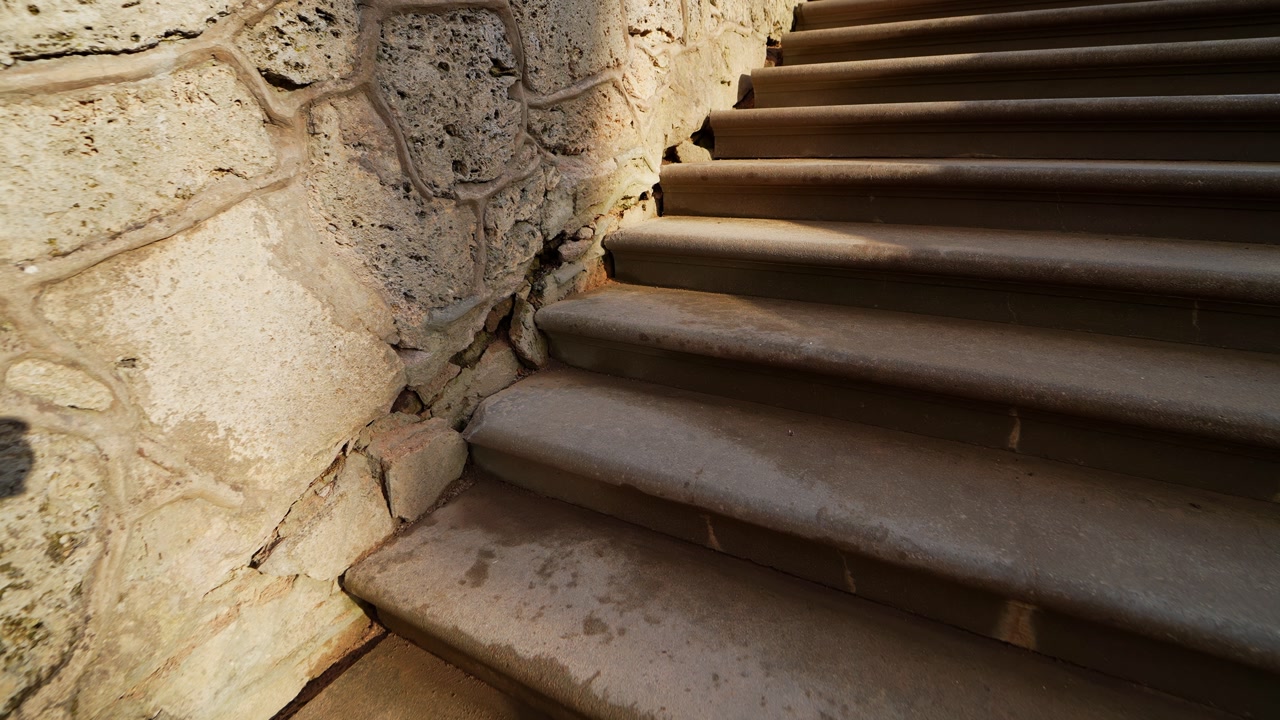 Close-up of worn stone stairs beside a cracked masonry wall, showing aged construction, surface wear, and historic architectural detail in warm sunlight.
