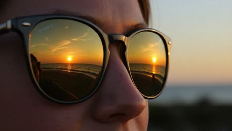 a stunning sunset reflected in sunglasses, capturing the vibrant colors of nature and the stillness of the evening sky by the beach