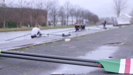 panning shot with female rowers preparing for a training session in single-scull and double-scull boats, with green white and red oar in the foreground sport fitness