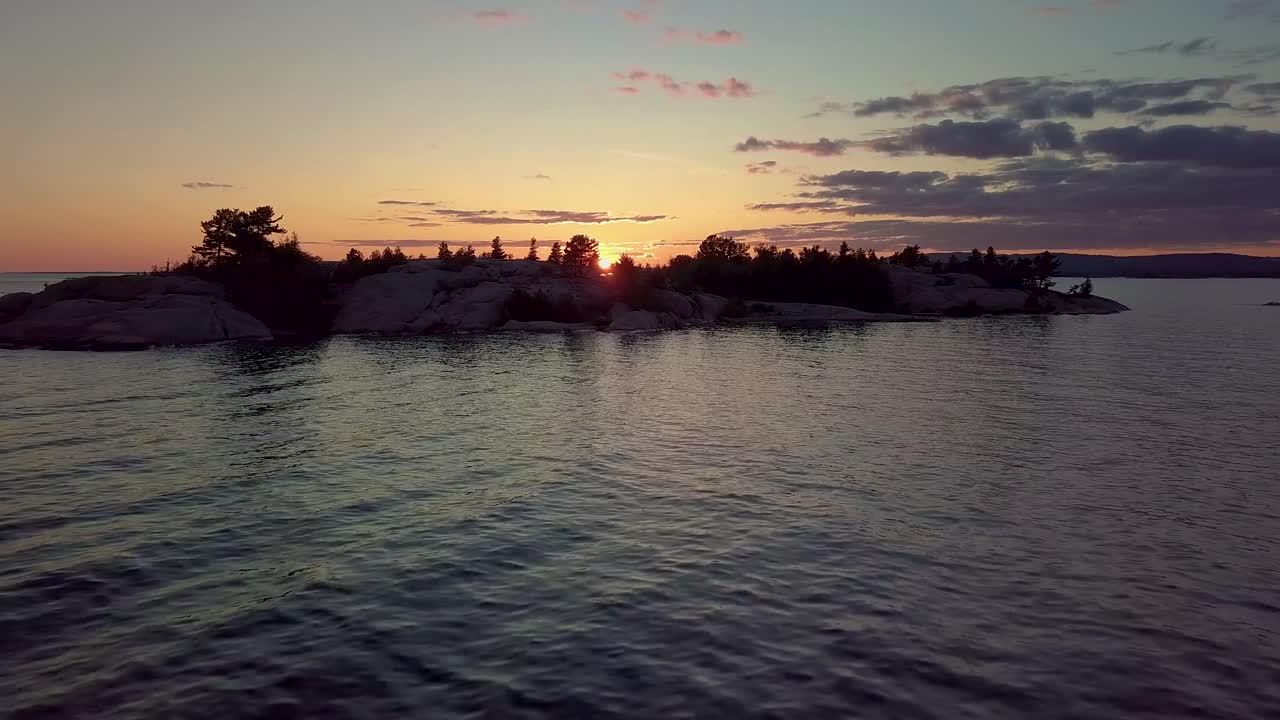 volando sobre las olas a la isla en el lago azul al atardecer, plataforma rodante aérea de drones en
