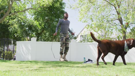 african american male soldier exercising and jumping rope with dog in garden