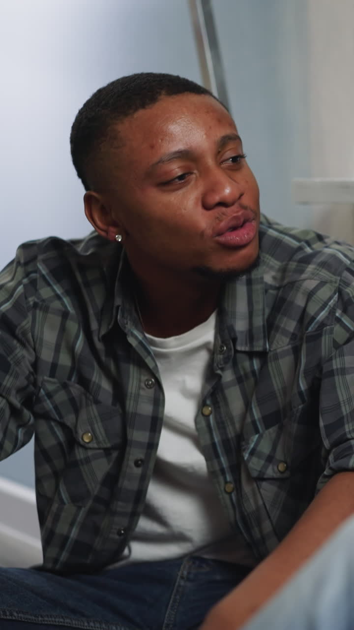 Young African-American man shares views on flat restoration with colleague sitting by window. Workers talk resting after wall painting in evening