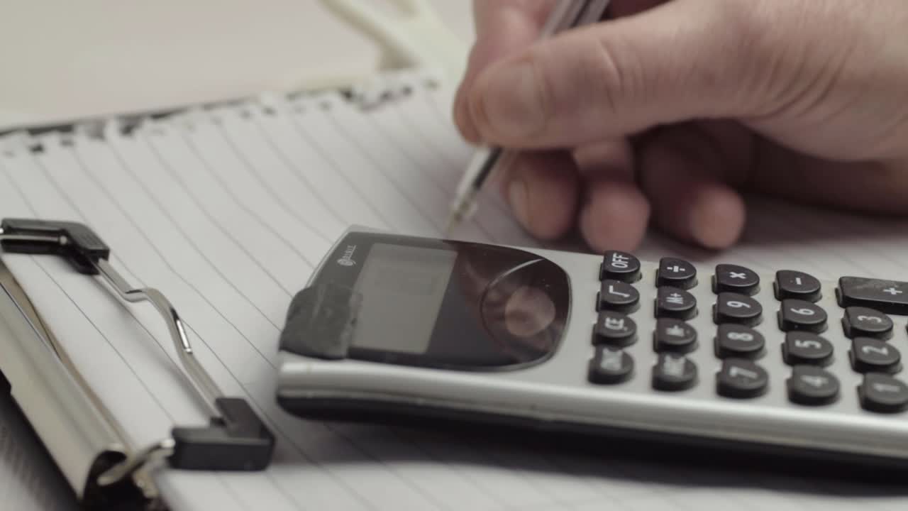 Hand writing financial information on clipboard with calculator medium shot