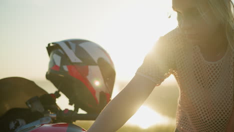 close-up of two women cleaning a motorcycle, one focusing on the task with the sun shining brightly behind her, the other woman is slightly blurred in the foreground