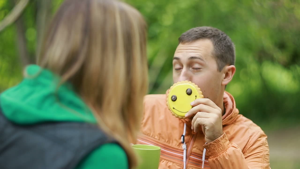 Couple Enjoying A Cup Of Tea. Happy young couple sitting on bench in park and drinking tea