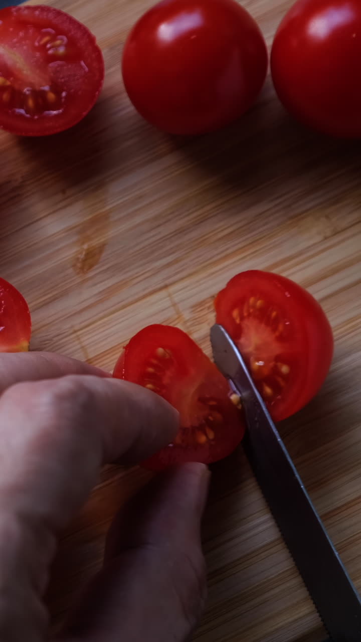 Top view of man hands cutting cherry tomatoes on the cutting board.