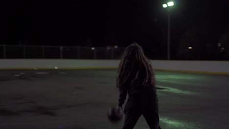 teenage girl dribbles ball then shoots it at net at an outdoor court at night