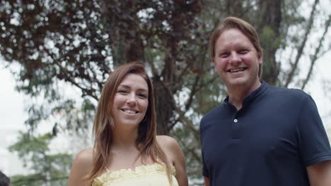 caucasian wife and husband looking at the camera, smiling, kissing and spending time together in nature on summer holidays