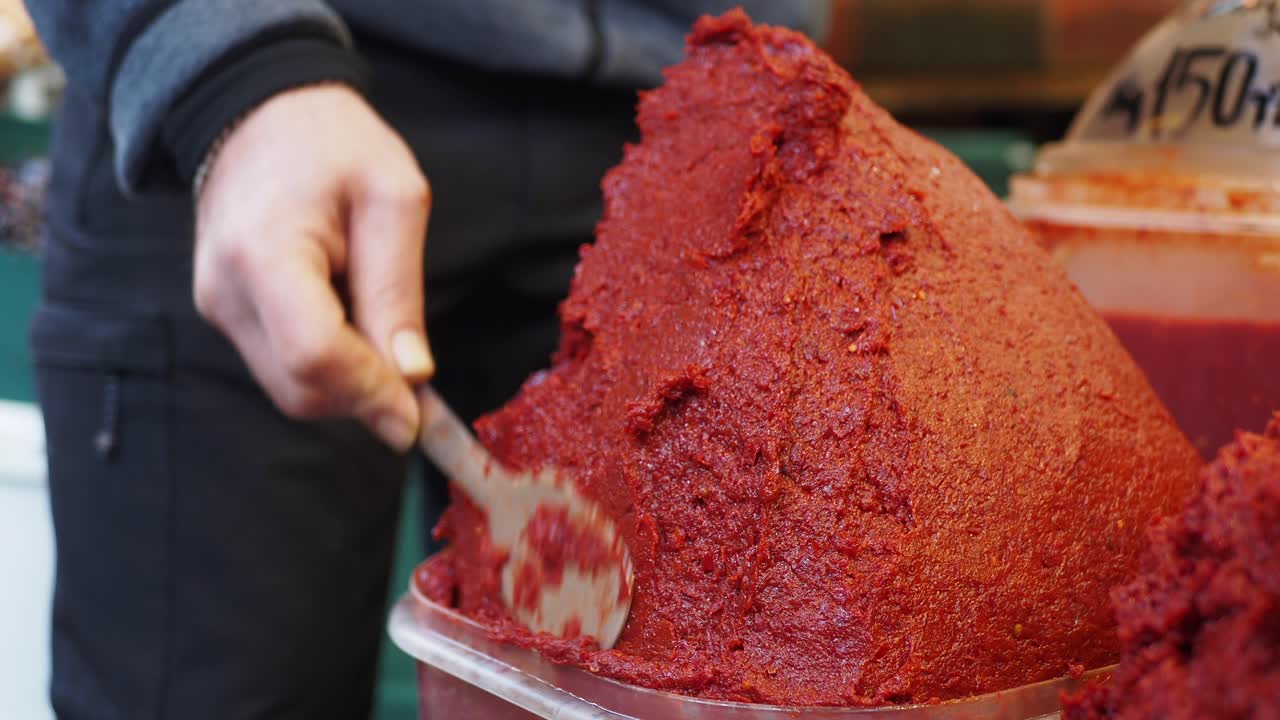 Persona sacando pasta de pimiento rojo de un recipiente en un mercado