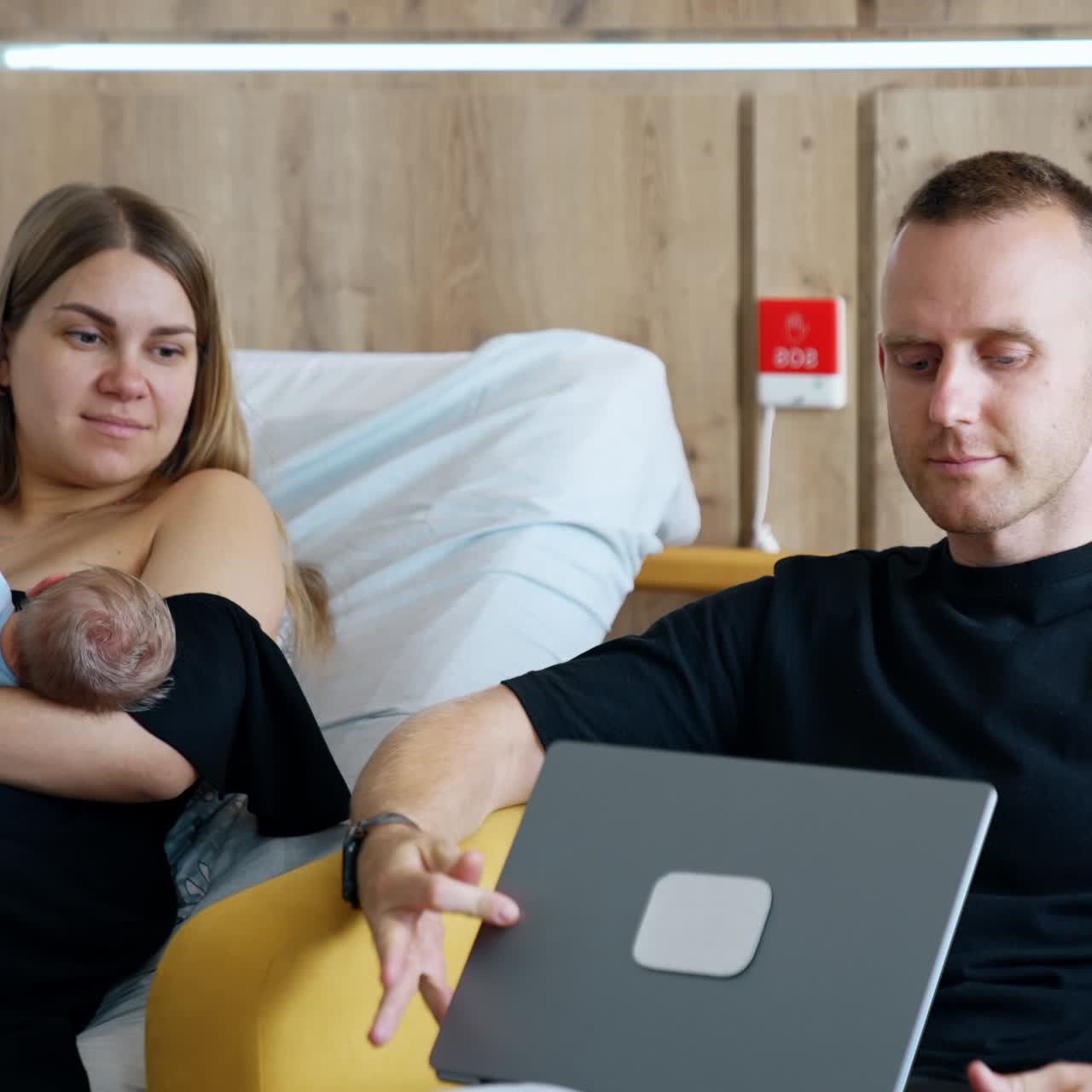 Husband finishes work at laptop and closes it. Man turns to his wife holding their newborn