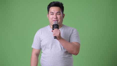 young handsome overweight asian man against green background