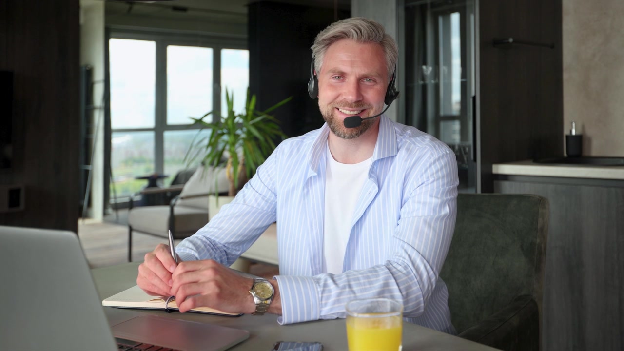 Smilende mand med headset taler under videoopkald fra hjemmekontor