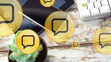 Animation of yellow digital message icons flying up over electronic devices on wooden background