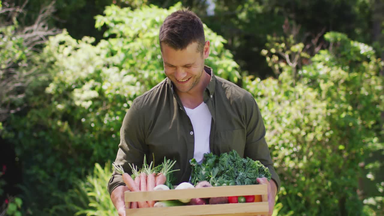 Portrait of caucasian man carrying a wooden tray full of vegetables in the garden