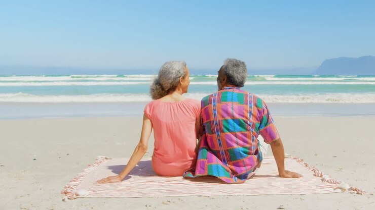 Rear view of active senior African American couple relaxing on blanket in the sunshine at beach 4k
