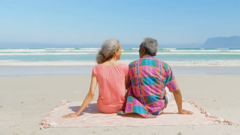 rear view of active senior african american couple relaxing on blanket in the sunshine at beach 4k