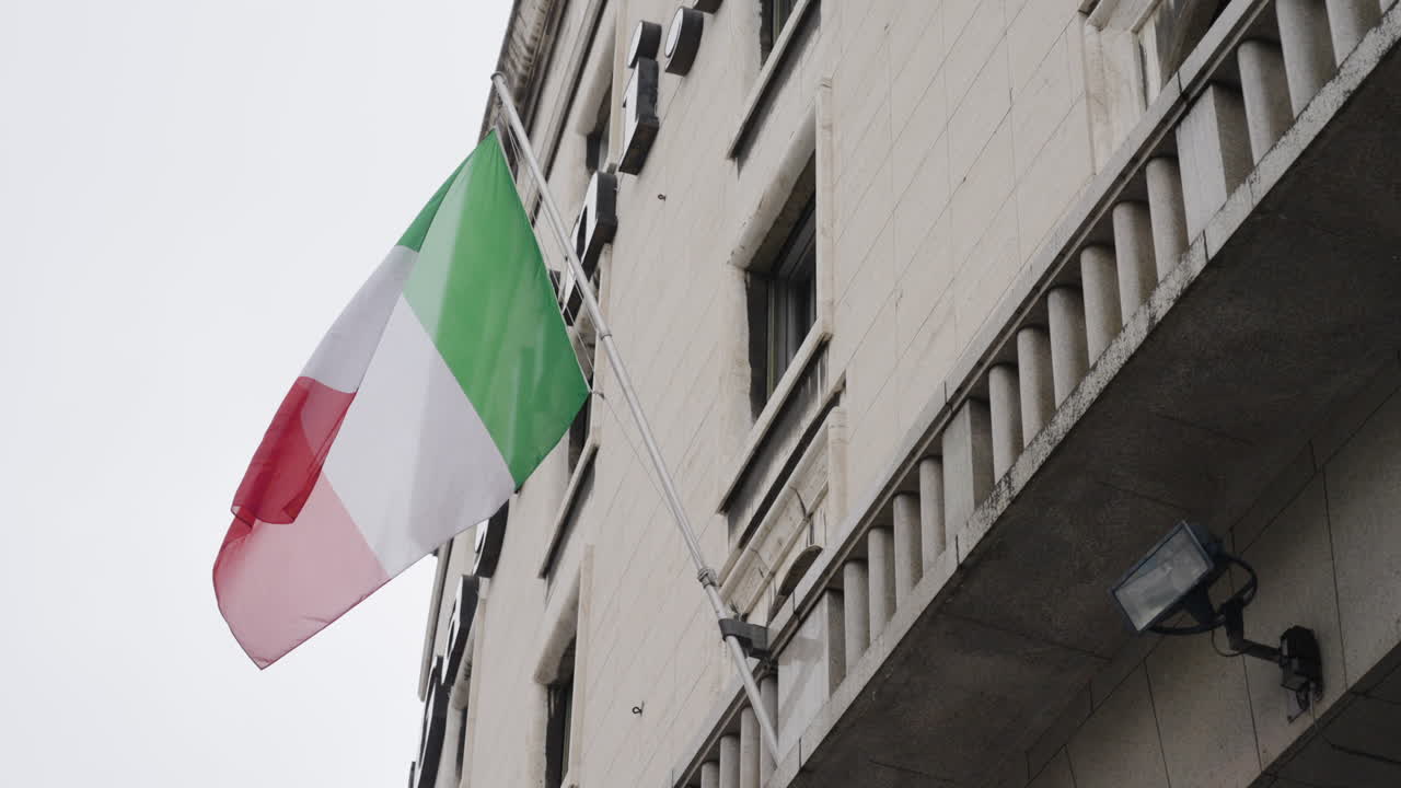 Bandiera nazionale italiana che sventola al rallentatore sulla facciata di un edificio, ripresa a mano.