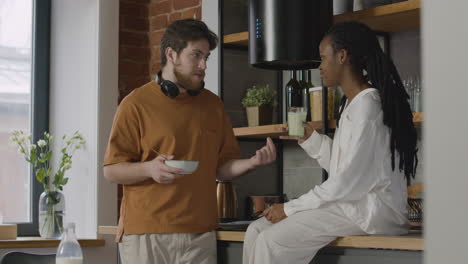 dos compañeros de cuarto desayunando y hablando juntos en la cocina de un piso compartido