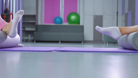 vista de las piernas de dos personas que participan en una sesión de fitness en esteras de yoga usando rodillos de espuma para ejercicios de piernas en un gimnasio bien iluminado, centrándose en el estiramiento y la recuperación muscular