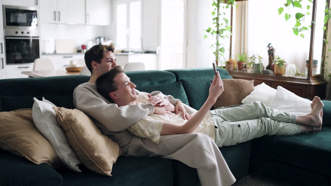 Liebevolles schwules Paar genießt Videoanruf auf dem Sofa zu Hause