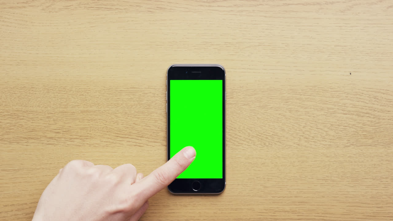Vista dall'alto: mani che usano un telefono cellulare touchscreen con gesti multi-touch su schermo verde, su una scrivania in legno - Red Epic Dragon