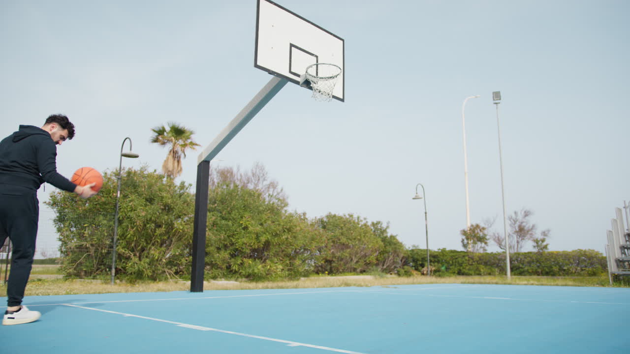 Uomo si diverte giocando a basket da solo sul campo all'aperto