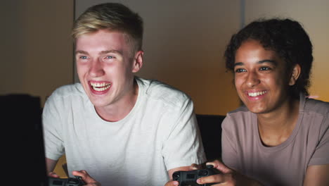 teenage girl beating boy as they sit on sofa at home playing computer game